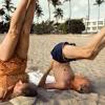 older people doing shoulder stand yoga pose on beach
